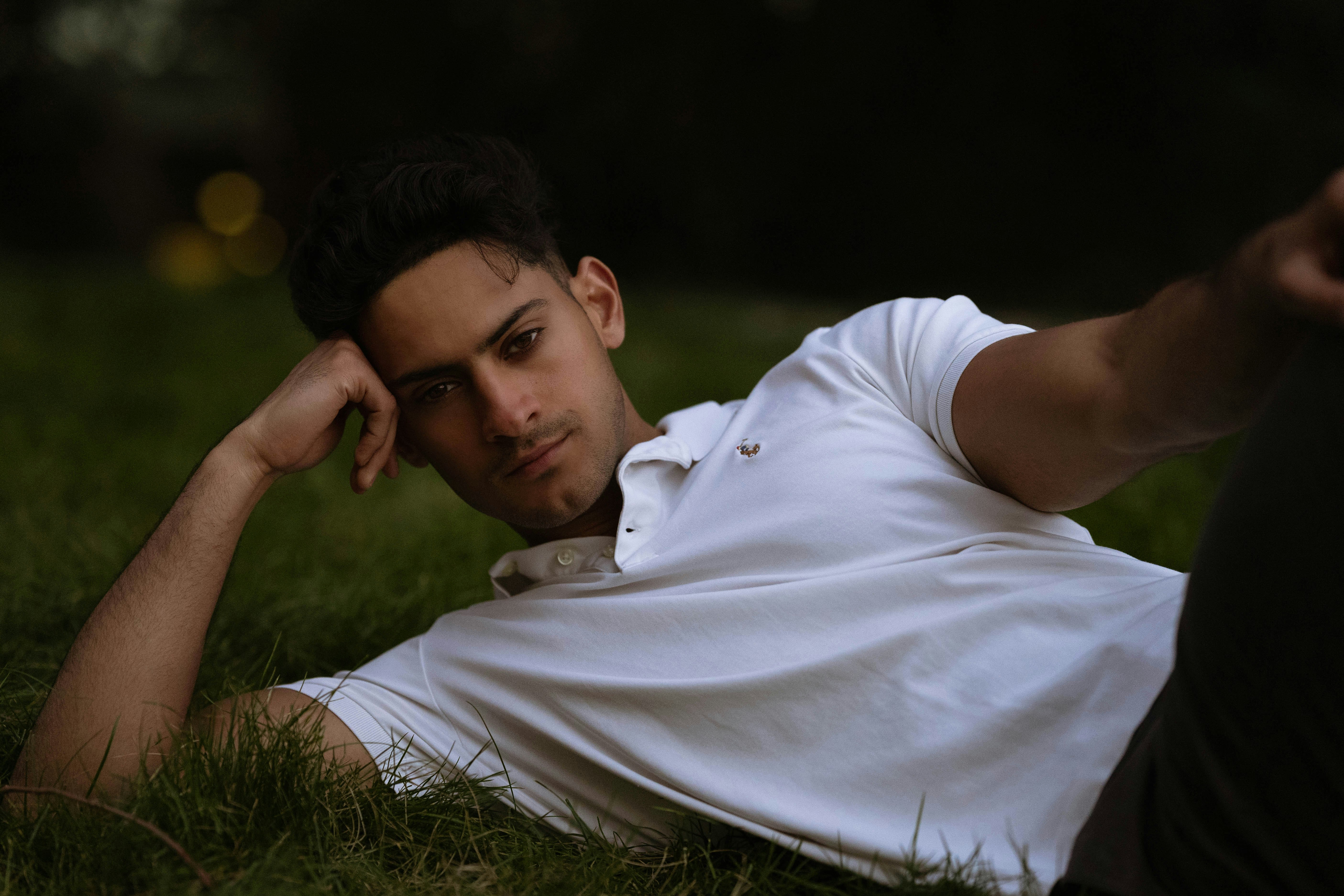 man in white polo shirt lying on green grass field